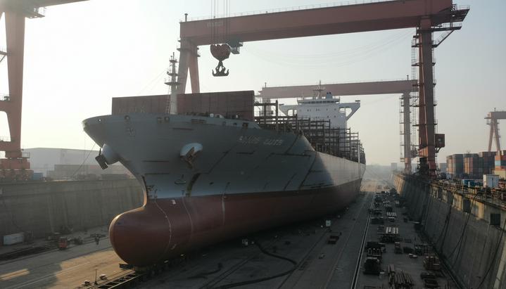 Minerva Marine: новый заказ на контейнеровозы в Китае Новый контейнеровоз в сухом доке китайской верфи на этапе строительства, окруженный портовыми кранами и строительными лесами.