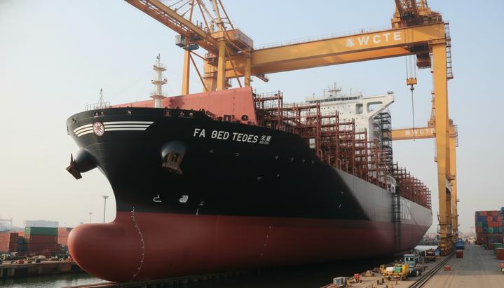 MSC продолжает экспансию: скупка судов для укрепления лидерства на море Огромный новый контейнеровоз на верфи, частично в строительных лесах, под высокими портовыми кранами в индустриальном пейзаже.